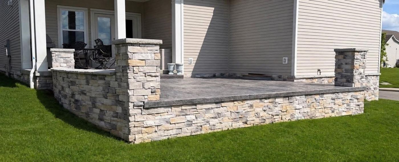 Raised stamped concrete porch with stacked stone veneer walls and pillars